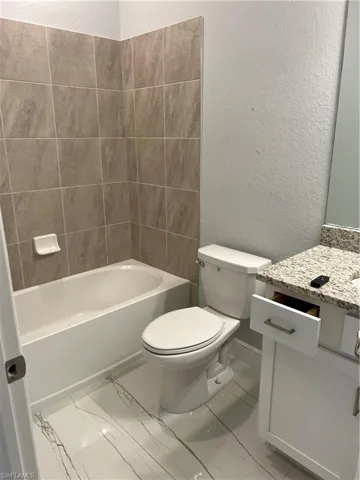Full bathroom with a textured wall, vanity, bathtub / shower combination, and light marble finish floors