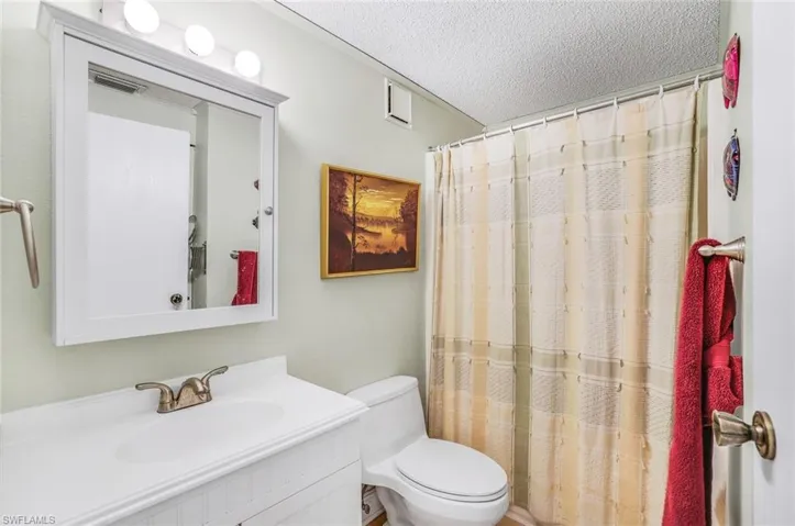 Bathroom featuring a textured ceiling, vanity, walk in shower, and toilet
