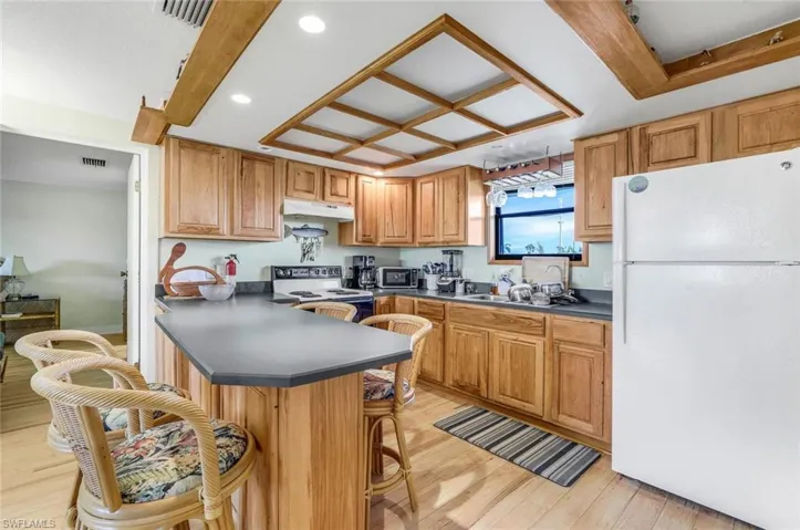 Kitchen featuring kitchen peninsula, a breakfast bar area, light hardwood / wood-style floors, and white appliances