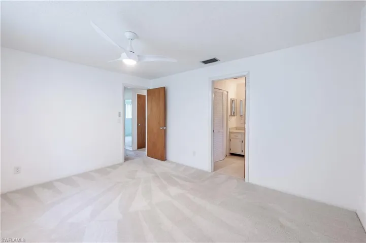 Unfurnished bedroom featuring light colored carpet, ensuite bathroom, and a ceiling fan