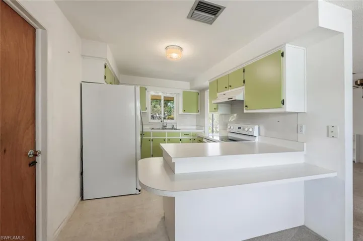 Kitchen with white appliances, a peninsula, light countertops, under cabinet range hood, and green cabinetry