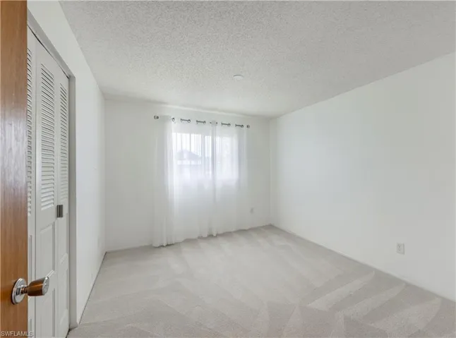 Unfurnished bedroom featuring light colored carpet, a closet, and a textured ceiling