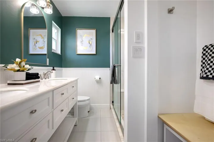 Full primary bathroom featuring double vanity, wainscoting, a shower stall, and light tile patterned floors