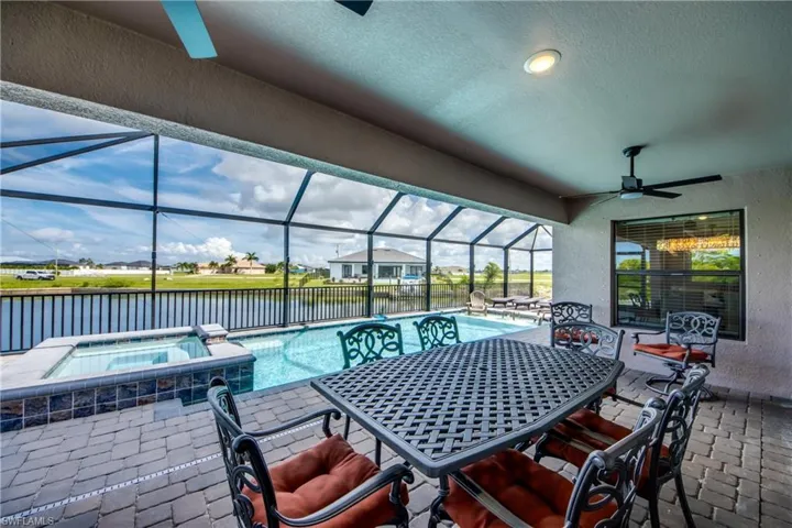 View of patio / terrace featuring a ceiling fan, outdoor dining space, a water view, a pool with connected hot tub, and a lanai