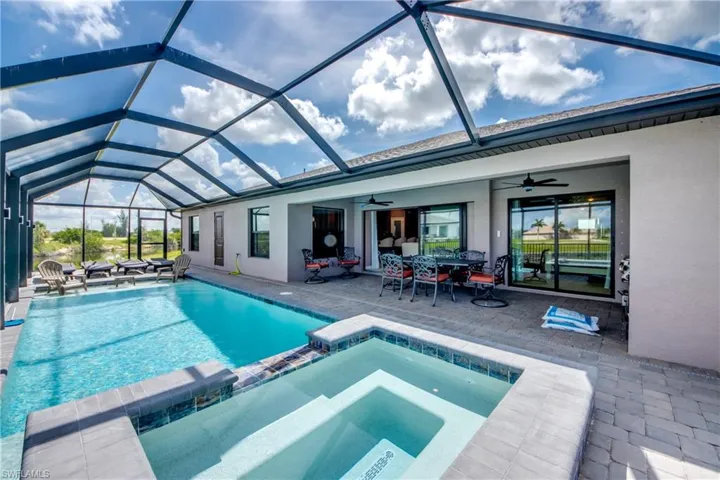 View of pool with a ceiling fan, a pool with connected hot tub, a patio, glass enclosure, and outdoor dining space