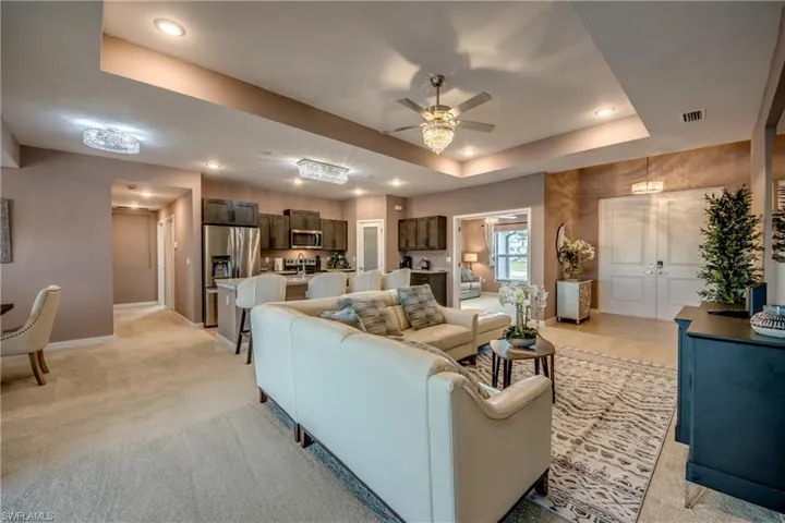 Living area with a raised ceiling, a ceiling fan, recessed lighting, and light colored carpet