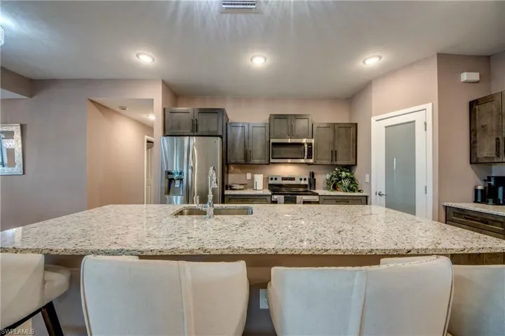 Kitchen featuring stainless steel appliances, a kitchen bar, an island with sink, light stone countertops, and recessed lighting