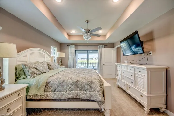 Bedroom featuring a raised ceiling, light colored carpet, connected bathroom, ceiling fan, and recessed lighting