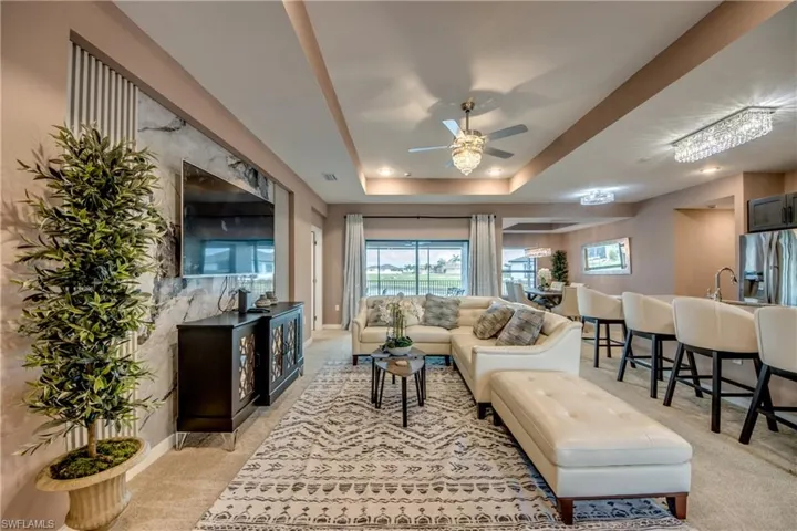 Living room with a tray ceiling, light colored carpet, and ceiling fan