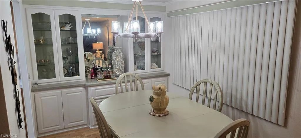 Dining space featuring a central chandelier with glass shades, built-in cabinetry with glass-front uppers, a mirrored backsplash, and wood-finish flooring