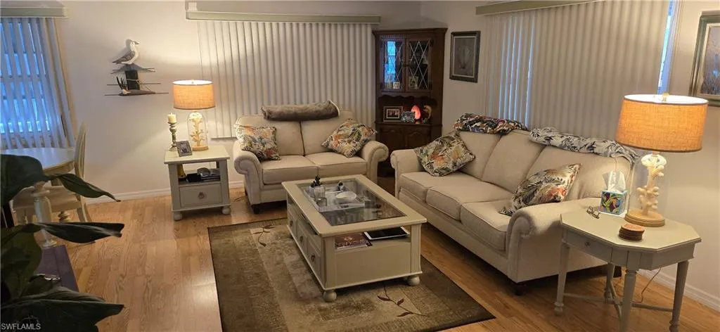 Open living area featuring wood-finish flooring, vertical blinds, and a built-in corner display cabinet