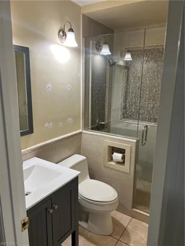 Bathroom featuring tile walls, vanity, a shower stall, light tile patterned flooring, and wainscoting