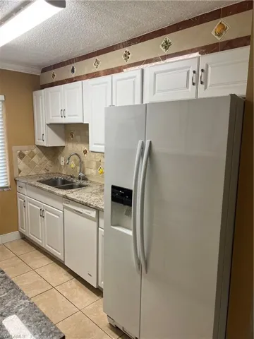 Kitchen with stainless steel fridge, white cabinets, dishwashing machine, light stone counters, and light tile patterned flooring
