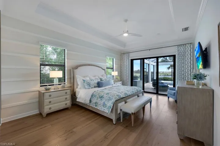 Bedroom featuring access to outside, light wood-type flooring, a tray ceiling, ceiling fan, and crown molding
