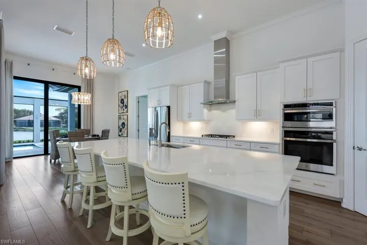 Kitchen with sink, an island with sink, wall chimney range hood, and decorative light fixtures