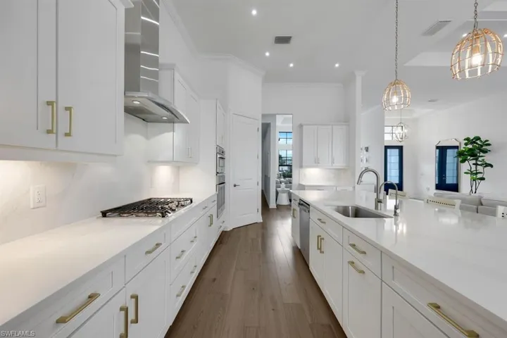 Kitchen with wall chimney range hood, hanging light fixtures, dark hardwood / wood-style flooring, stainless steel appliances, and sink