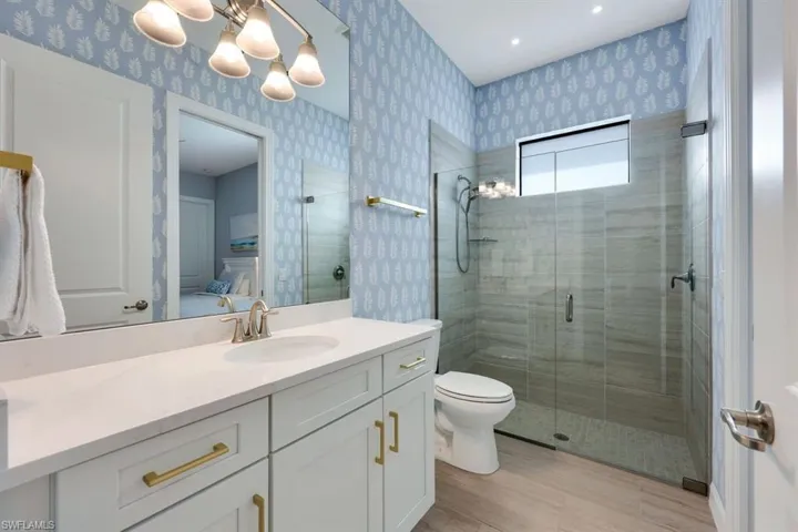 Bathroom featuring a shower with door, hardwood / wood-style floors, toilet, vanity, and a notable chandelier