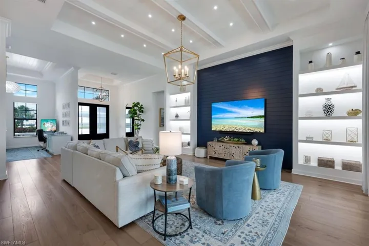 Living room featuring a notable chandelier, wood-type flooring, beamed ceiling, built in shelves, and french doors