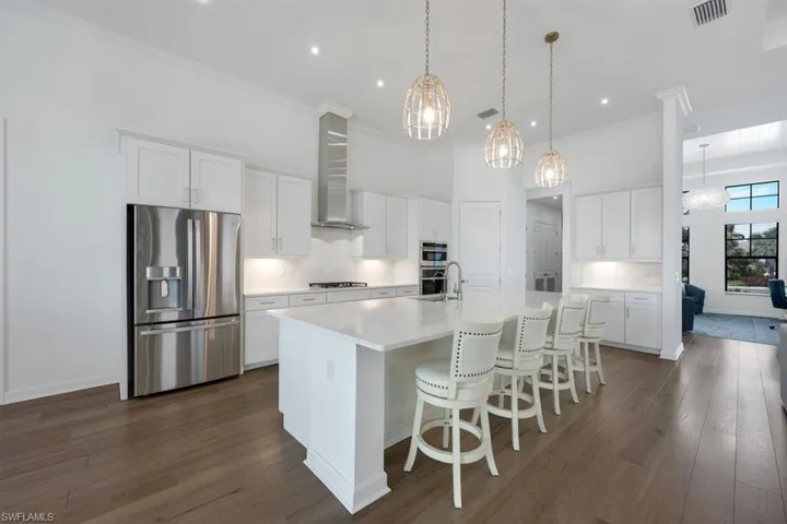 Kitchen with stainless steel appliances, wall chimney exhaust hood, a center island with sink, and white cabinets