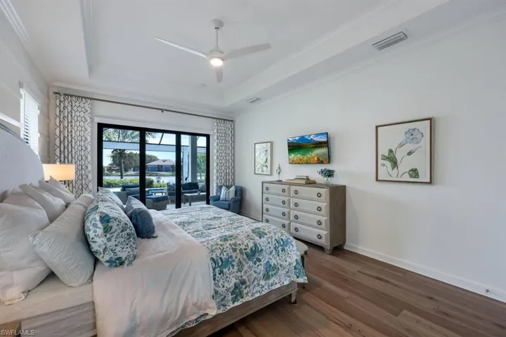 Bedroom with hardwood / wood-style floors, ceiling fan, access to outside, a tray ceiling, and crown molding