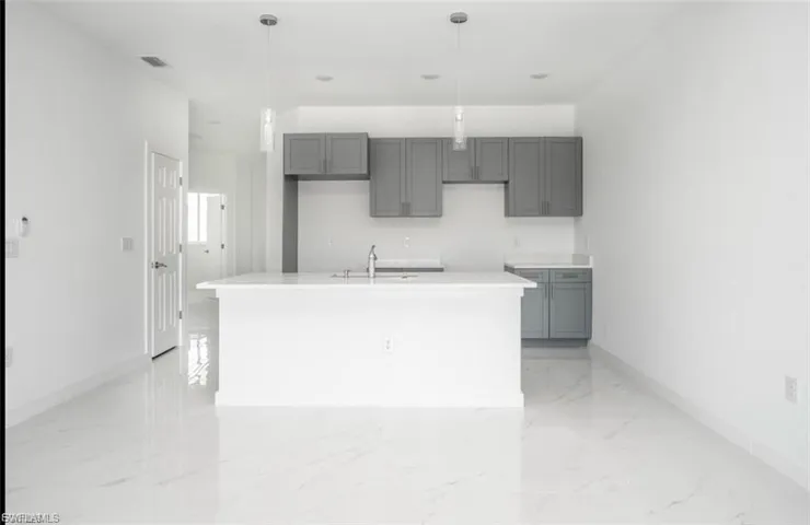 Kitchen featuring gray cabinets, an island with sink, pendant lighting, light marble finish flooring, and light stone countertops