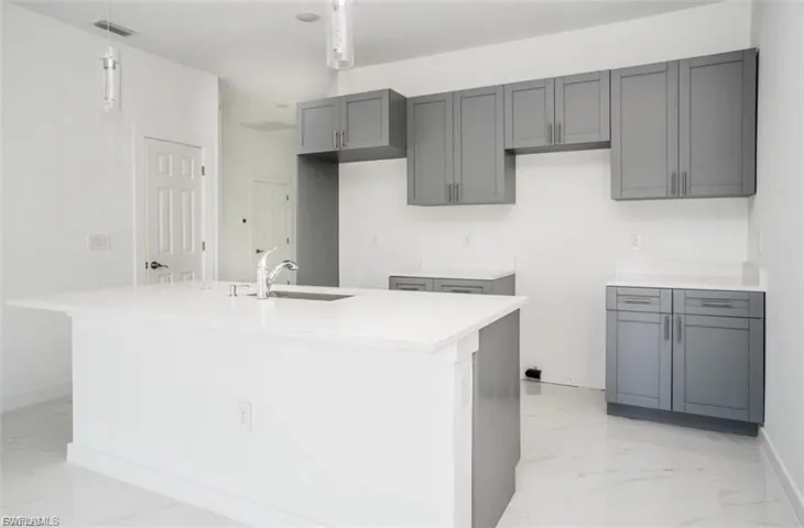 Kitchen with light marble finish flooring, gray cabinets, light stone countertops, and a center island with sink