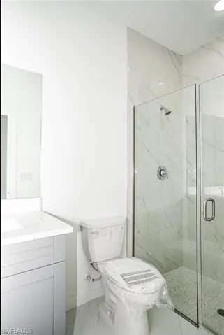 Full bath with light marble finish flooring, a marble finish shower, and vanity