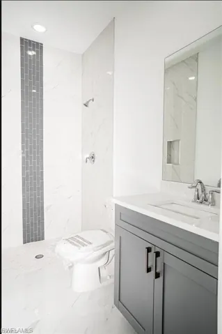 Full bath with vanity, a marble finish shower, light marble finish flooring, and recessed lighting