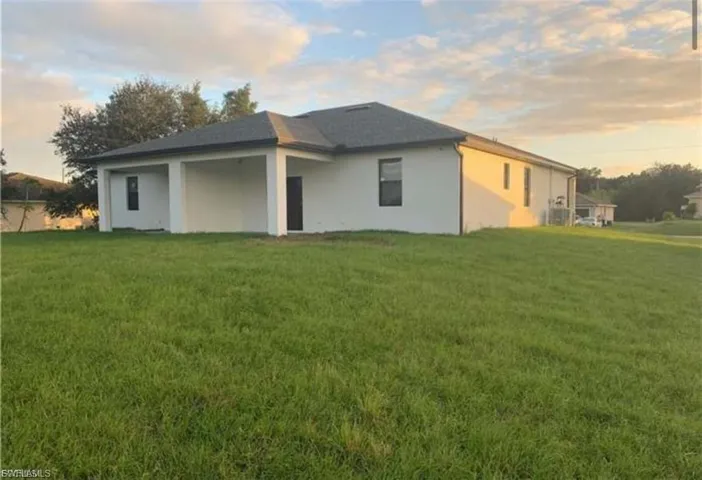 Rear view of house featuring a lawn and stucco siding