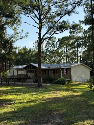 Expansive front yard with mature trees, covered front porch, and wood railing