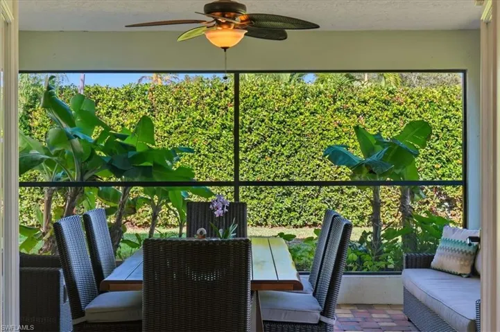 Screened patio featuring a ceiling fan with integrated lighting, brick-patterned tile flooring, and a lush green hedge backdrop