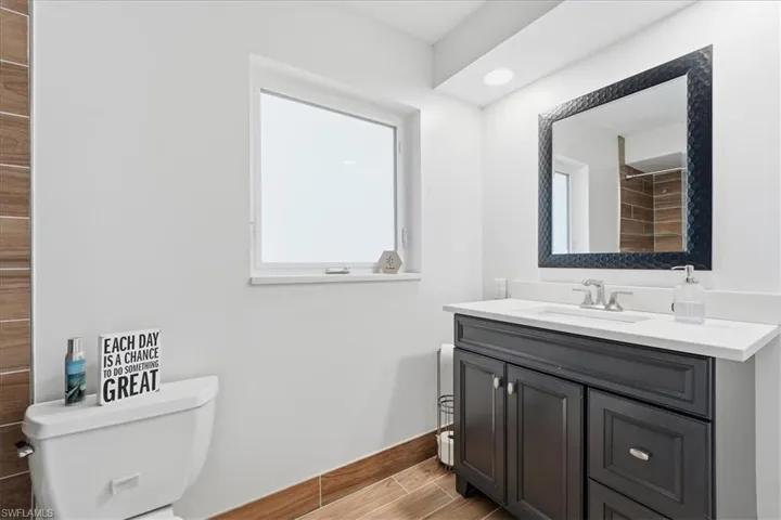 Bathroom featuring a dark wood-finish vanity with a light countertop, a rectangular mirror with a textured black frame, and a white toilet