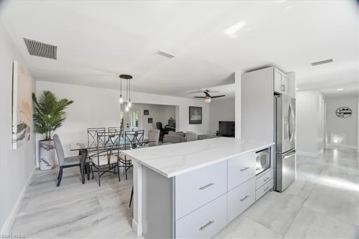 Open-concept kitchen and dining area featuring a quartz-finish island with integrated microwave, stainless steel appliances, contemporary light gray cabinetry, and light-toned tile flooring
