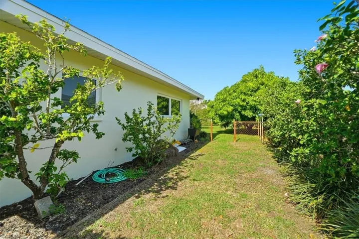 Side yard with a manicured lawn, established landscaping, and a partial chain-link fence