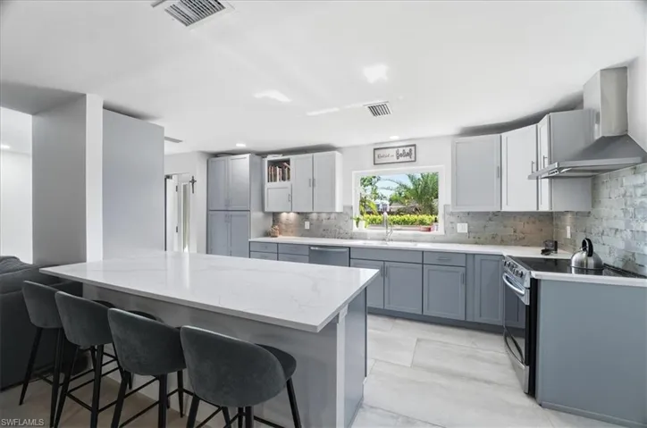 Spacious kitchen featuring a large island with a quartz countertop, gray cabinetry, stainless steel appliances, and a tiled backsplash