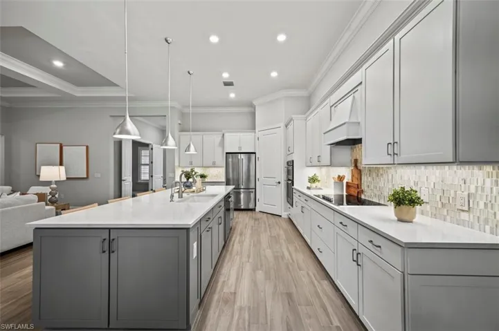 Kitchen featuring crown molding, pendant lighting, decorative backsplash, freestanding refrigerator, and light wood finished floors