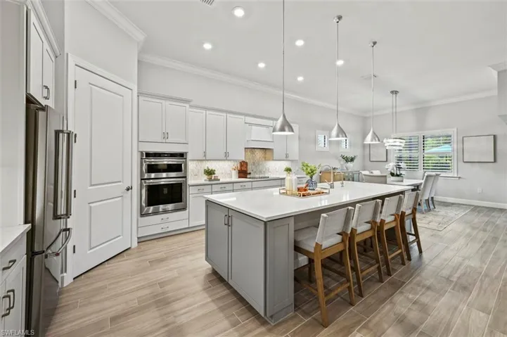 Kitchen featuring crown molding, a kitchen bar, decorative backsplash, an island with sink, and decorative light fixtures