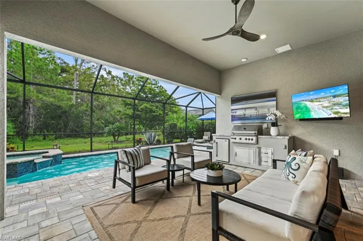 View of patio with exterior kitchen, a sunroom, a pool with connected hot tub, glass enclosure, and outdoor lounge area