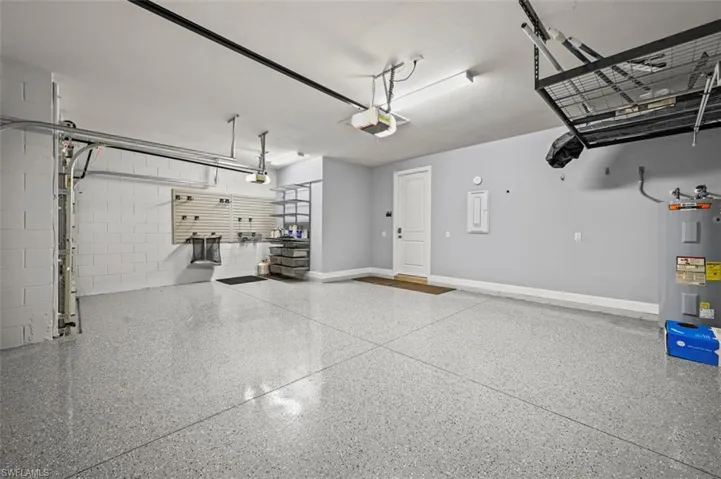 Garage with water heater, concrete block wall, and a garage door opener