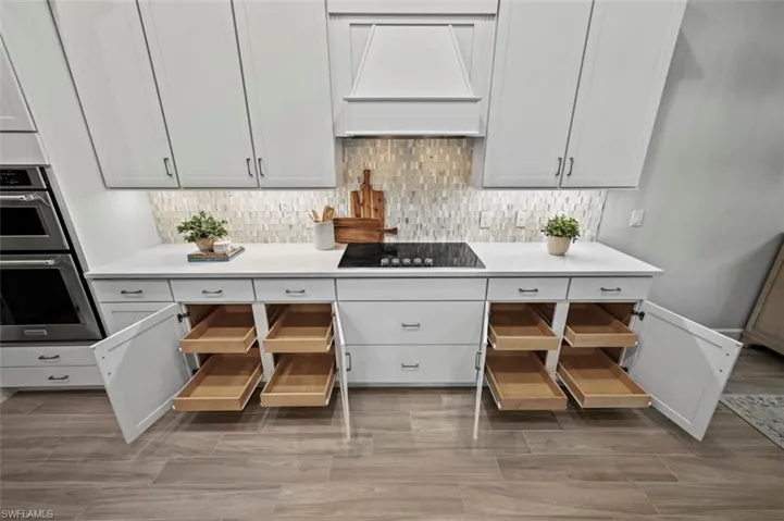 Kitchen with decorative backsplash, custom range hood, white cabinetry, wood tiled floors, and stainless steel double oven