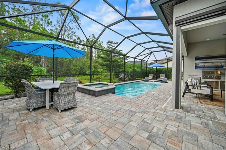 View of swimming pool with an outdoor kitchen, a sunroom, a patio, a pool with connected hot tub, and glass enclosure