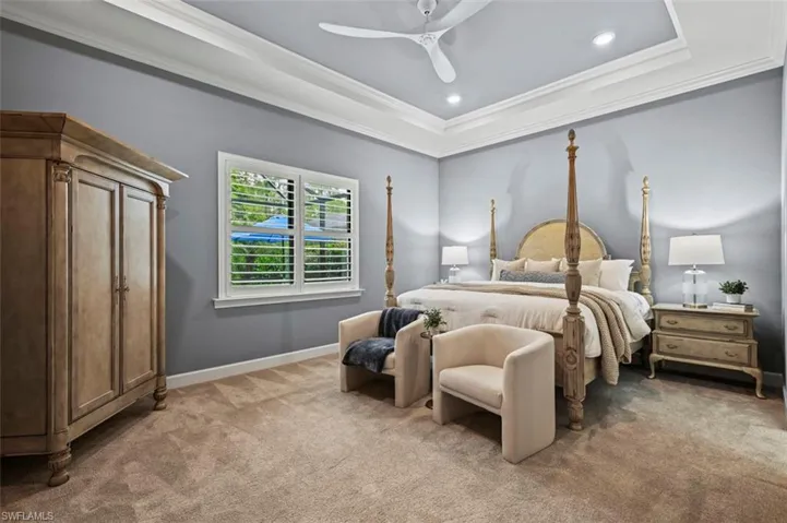 Bedroom featuring a raised ceiling, light carpet, recessed lighting, crown molding, and a ceiling fan