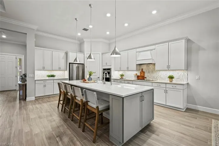 Kitchen with crown molding, a kitchen bar, a kitchen island with sink, white cabinets, and tasteful backsplash
