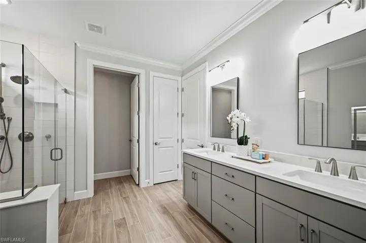 Full bathroom with a shower stall, double vanity, wood tiled floors, and crown molding