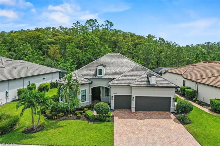 View of front of house with stucco siding, a front lawn, a garage, decorative driveway, and a forest view
