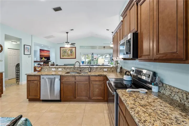 Kitchen with stainless steel appliances, light stone counters, light tile patterned floors, wood finish cabinetry, and a peninsula