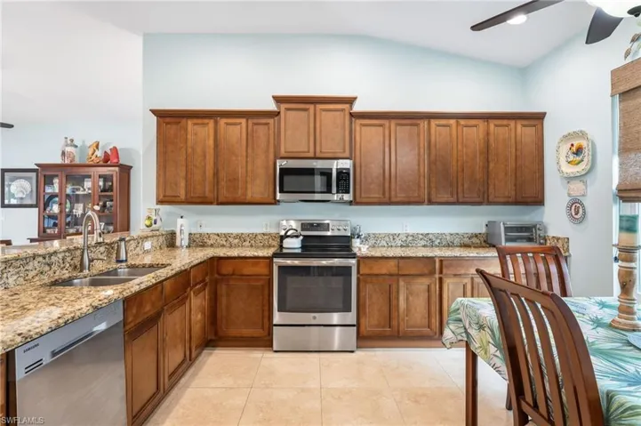 Kitchen with stainless steel appliances, wood finish cabinets, ceiling fan, light stone countertops, and lofted ceiling