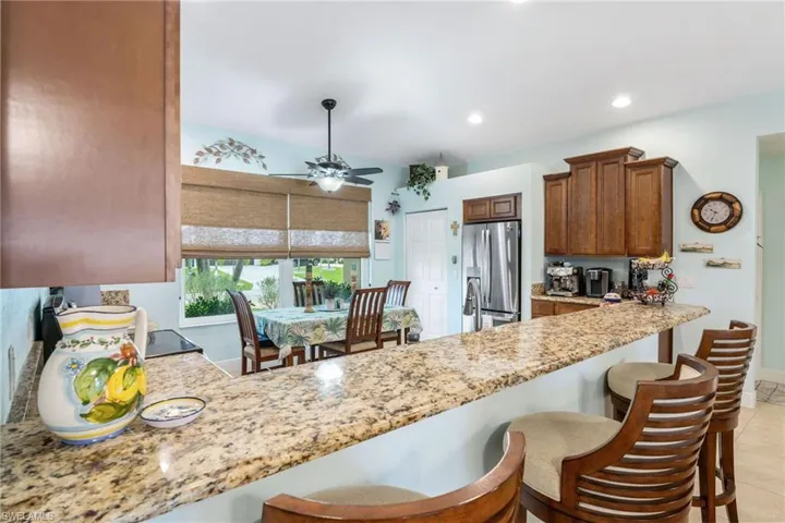 Kitchen featuring a breakfast bar area, stainless steel fridge with ice dispenser, light stone countertops, a peninsula, and recessed lighting
