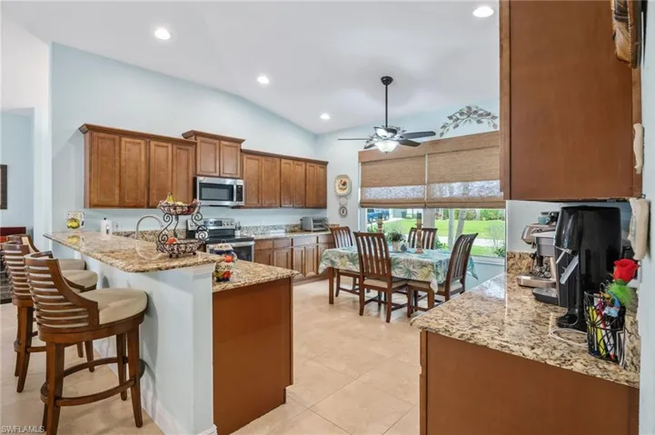 Kitchen with wood finish cabinets, light stone countertops, stainless steel appliances, vaulted ceiling, and a peninsula