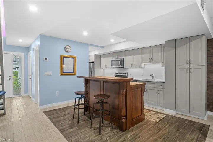 Kitchen featuring stainless steel appliances, wood tiled floors, a kitchen island, a breakfast bar area, and recessed lighting